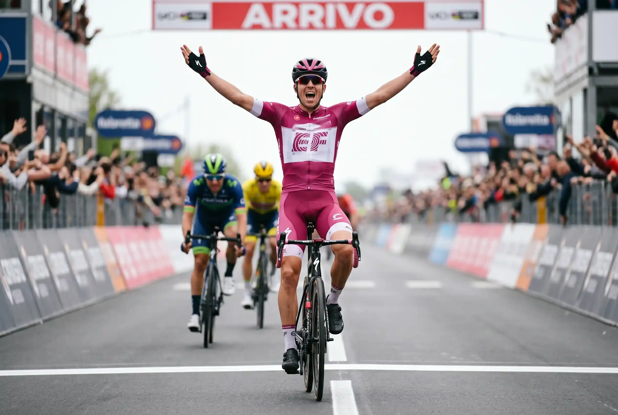 Ciclista professionista taglia il traguardo a braccia alzate dopo la vittoria di tappa in una corsa UCI World Tour